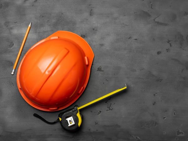Orange hardhat, ruler and pencil on black background top view